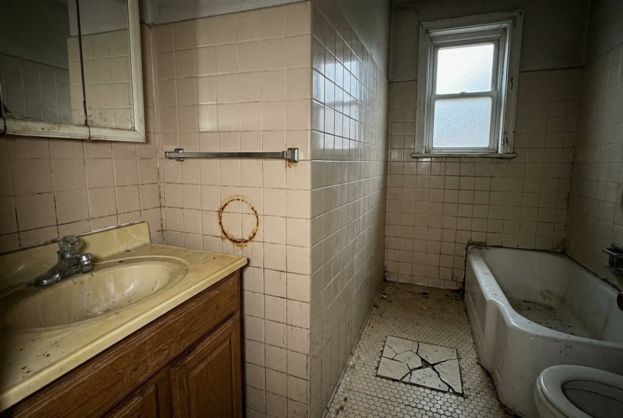 Grimy dated bathroom with cracked tile and rusted fixtures