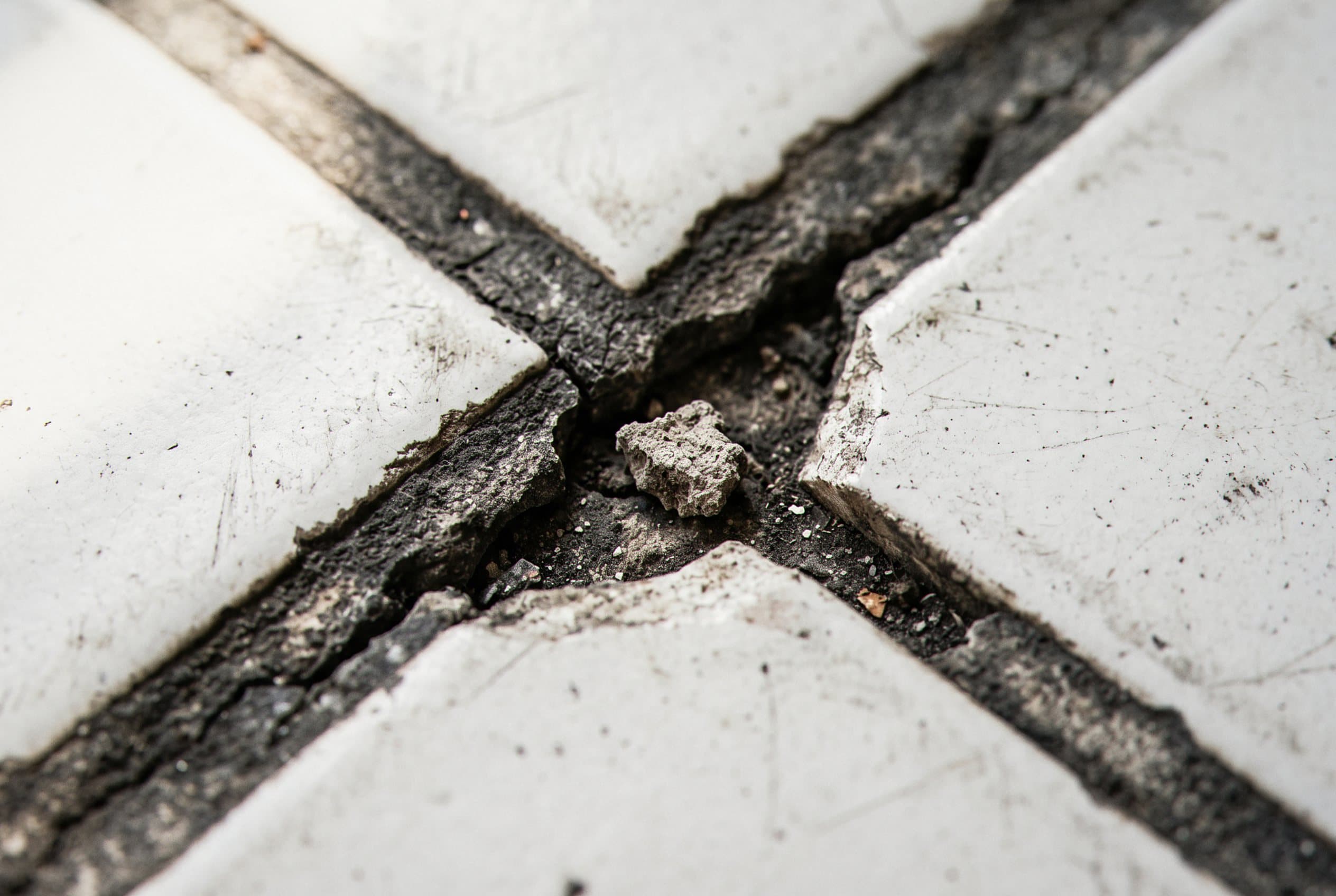 Cracked grout joint between white floor tiles