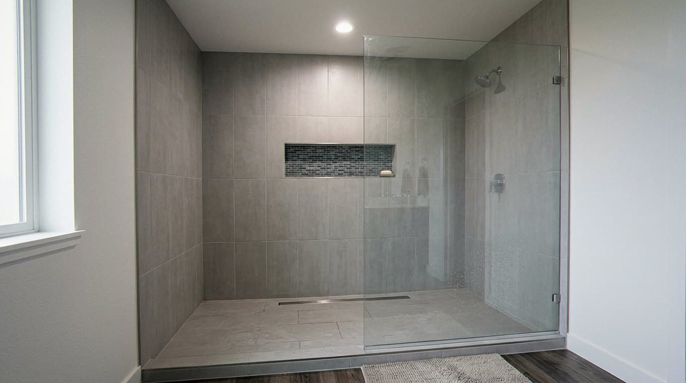 Glass-enclosed shower with large gray tile and rain head
