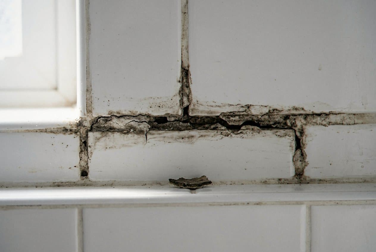 Cracked blackened grout on a white tile backsplash