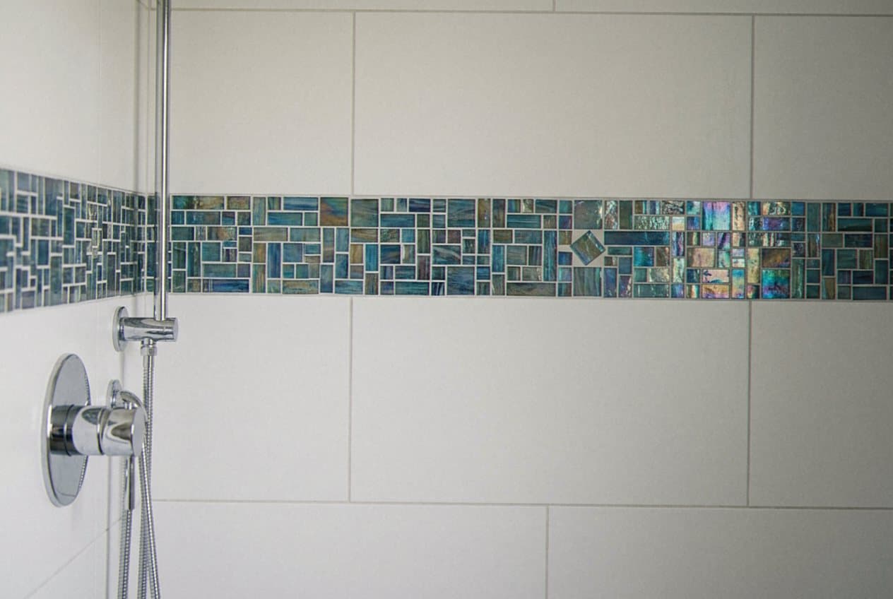 Iridescent glass mosaic accent band across a shower wall